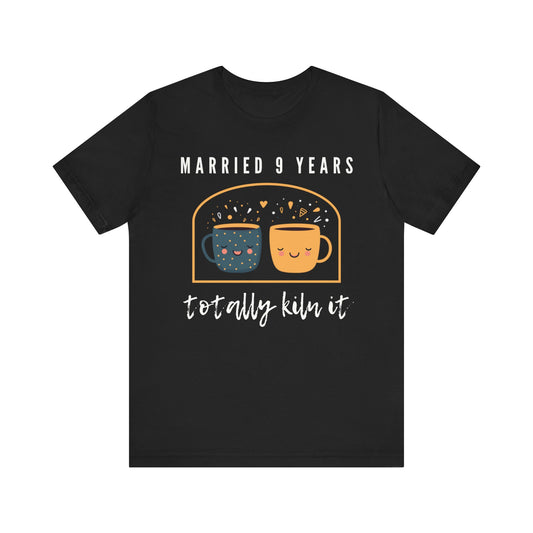 Black anniversary t-shirt with the text Married 9 Years Totally Kiln It around two cartoon cups in a pottery kiln